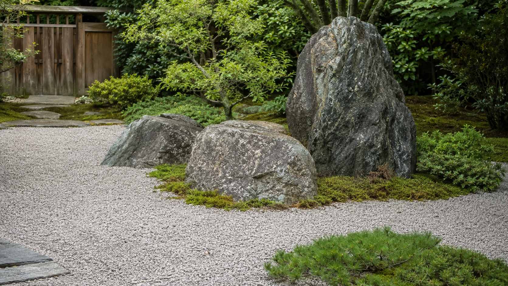 Large natural rocks used as a focal point in a peaceful Japanese garden with gravel, moss, and low shrubs.
