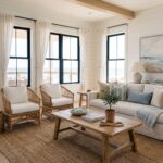 Beach house interior living room with white walls, large windows, natural light, linen seating, rattan accents, and soft coastal colors.
