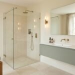 Modern bathroom with neutral walls, sage green vanity, blue-gray accents, wood, and brass fixtures.
